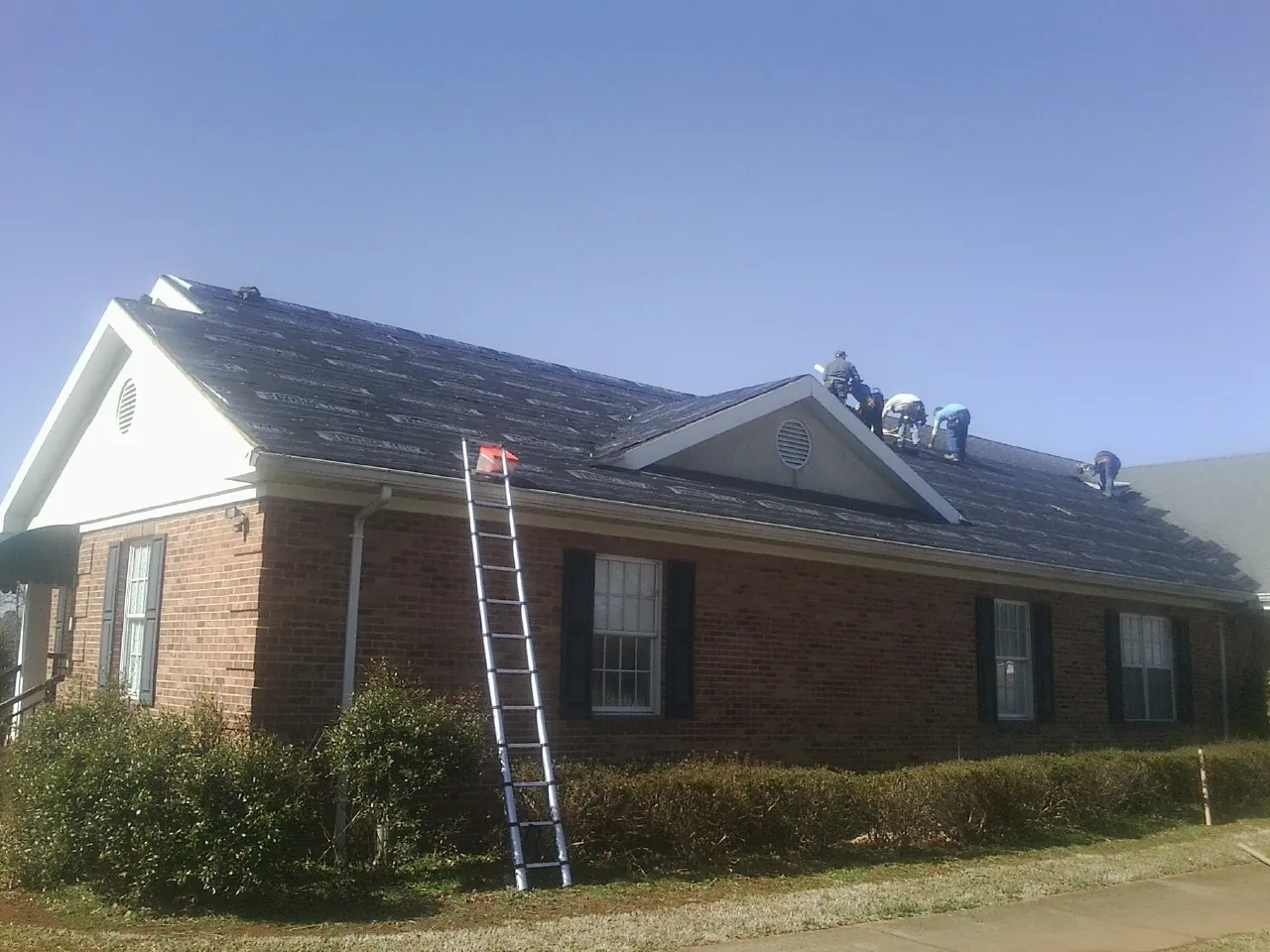 Crew tearing shingles off a brick ranch roof with a ladder set — Emergency Roof Repair work by our crew in Henderson