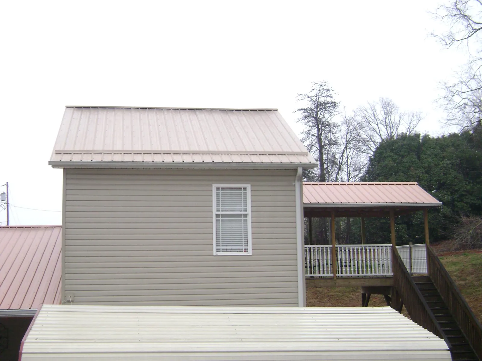 Tan metal roofs on a two story addition and attached porch, from a Roof Replacement job in Henderson